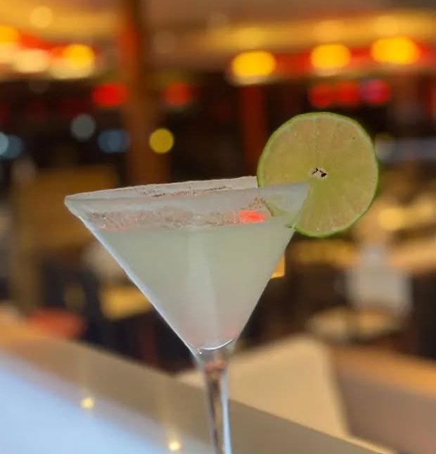 Margarita com rodela de lima sobre o balcão do bar, com a sala desfocada atrás