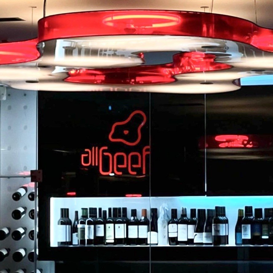 Balcão do bar com garrafas de vinho, o logótipo em néon vermelho e candeeiros vermelhos no teto